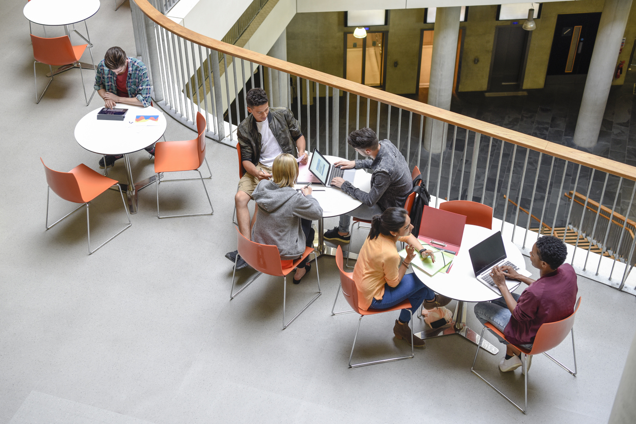 Students sitting at tables using laptops and meeting friends